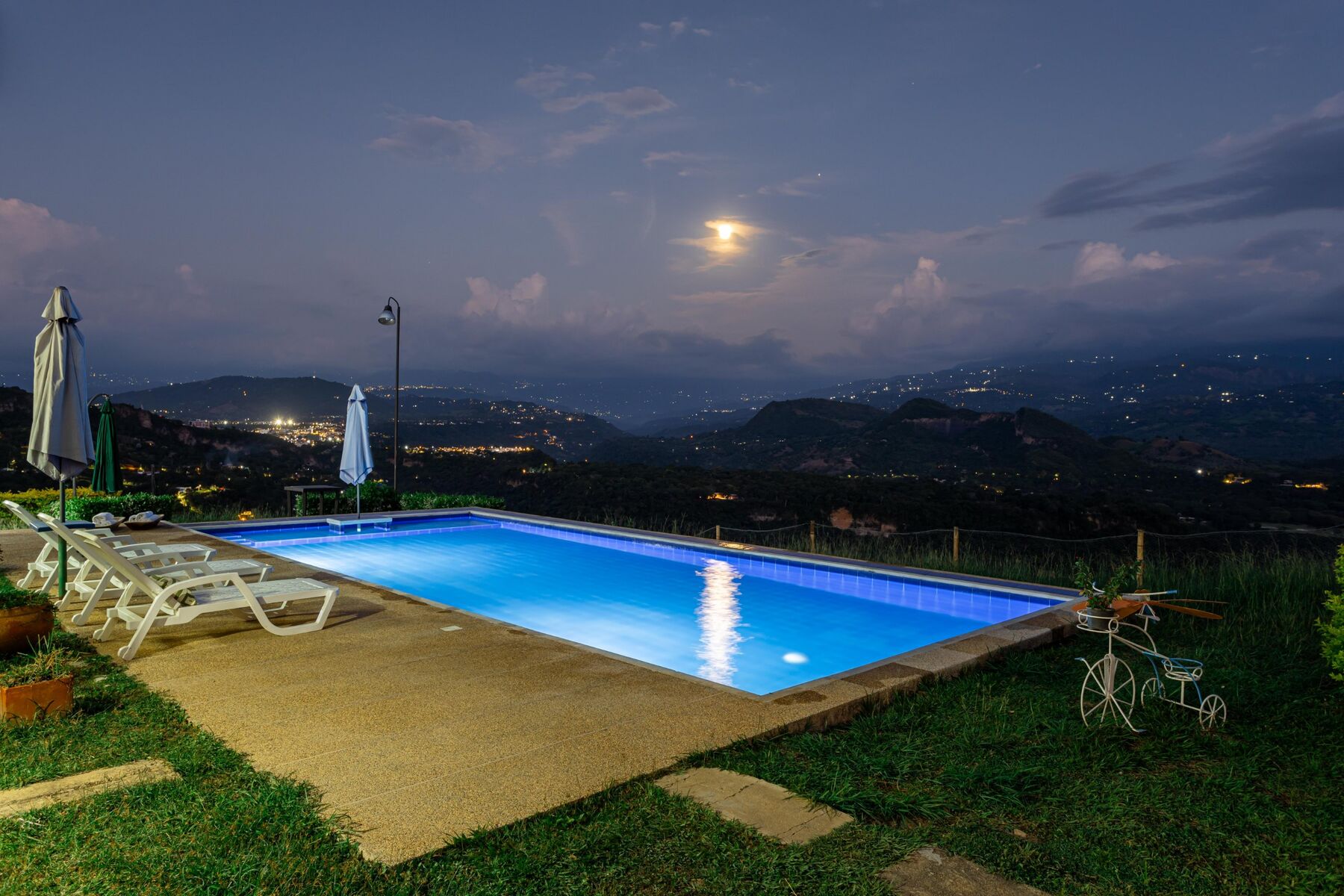 Piscina iluminada bajo la luna llena con vista a las montañas en El Encanto, Anapoima