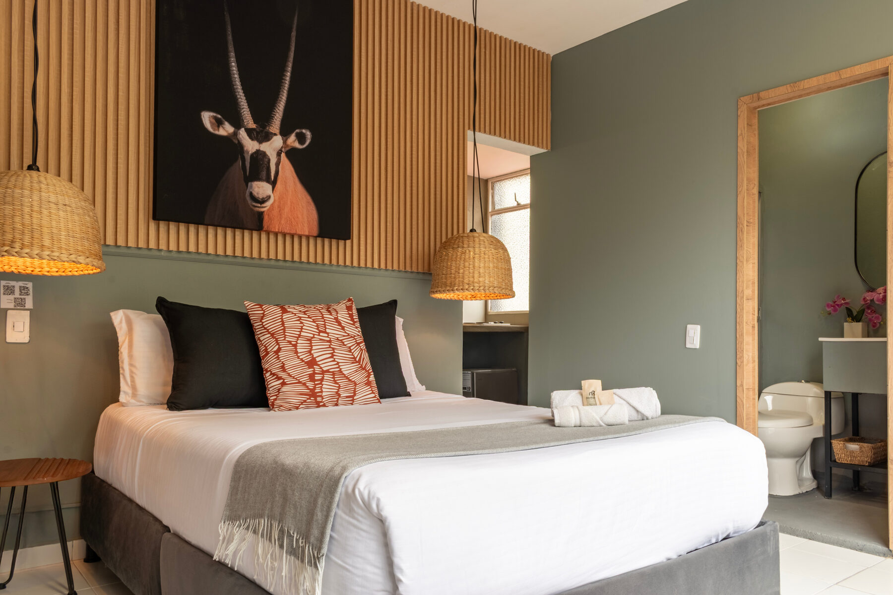 Habitación con cabecero de listones de madera, lámpara de mimbre y arte de un órice